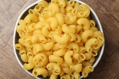 Photo of Raw horns pasta in bowl on wooden table, top view