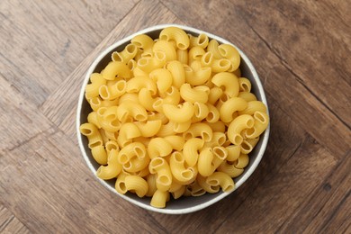 Photo of Raw horns pasta in bowl on wooden table, top view