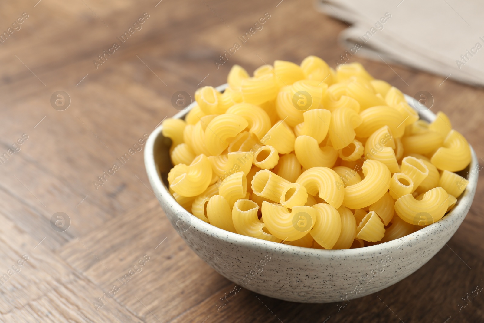 Photo of Raw horns pasta in bowl on wooden table, closeup