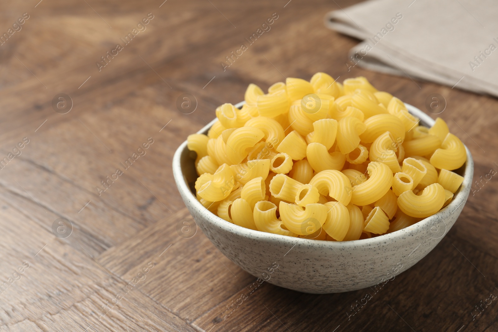 Photo of Raw horns pasta in bowl on wooden table, closeup