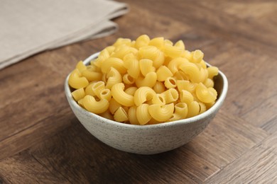 Photo of Raw horns pasta in bowl on wooden table, closeup