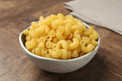 Photo of Raw horns pasta in bowl on wooden table, closeup