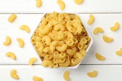 Photo of Raw horns pasta in bowl on white wooden table, top view