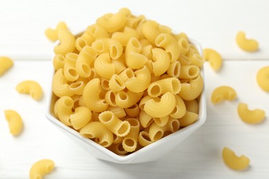 Photo of Raw horns pasta in bowl on white table, closeup