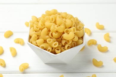 Photo of Raw horns pasta in bowl on white wooden table, closeup