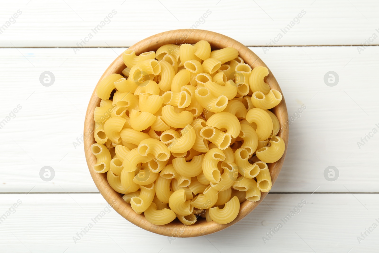 Photo of Raw horns pasta in bowl on white wooden table, top view