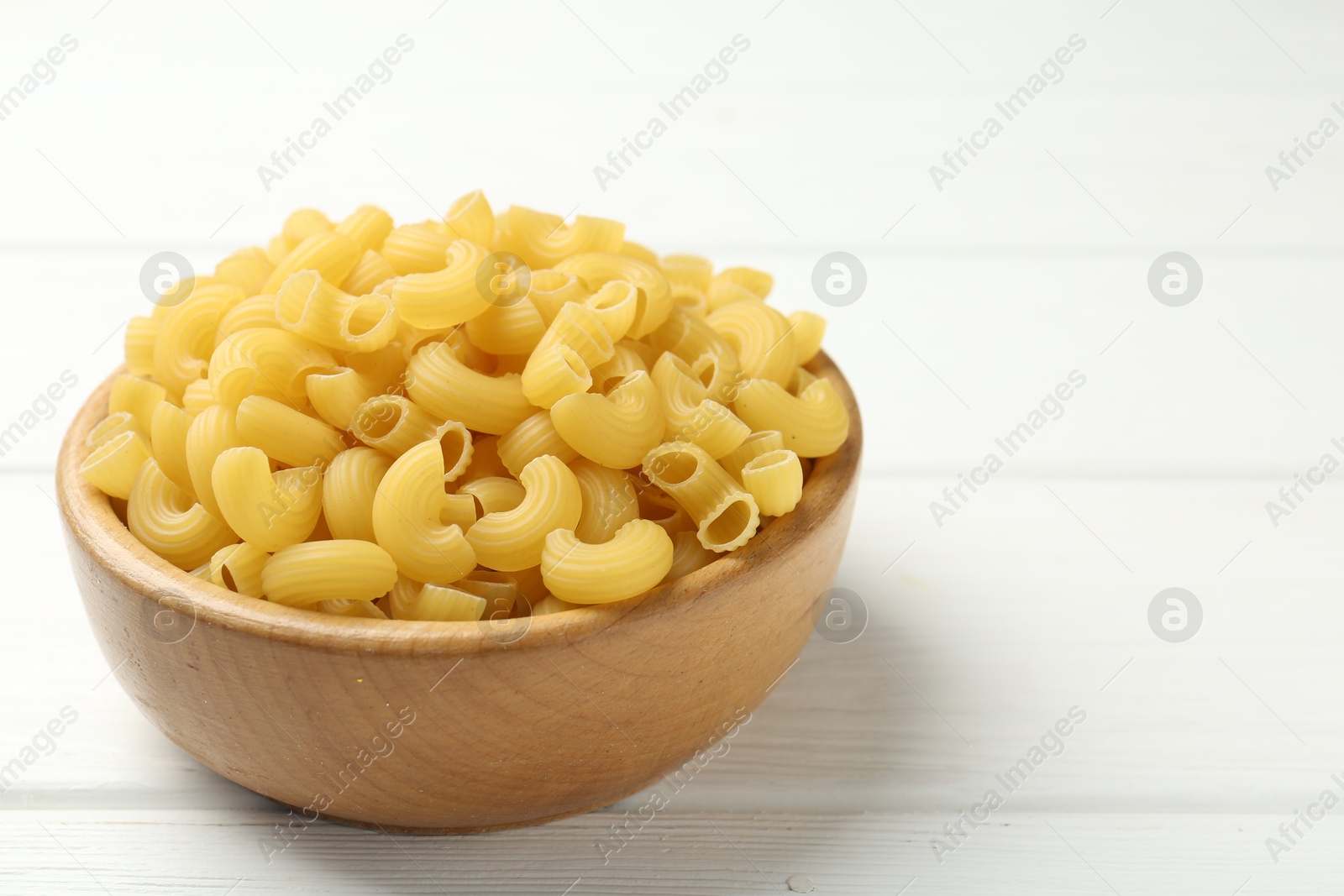 Photo of Raw horns pasta in bowl on white wooden table, closeup