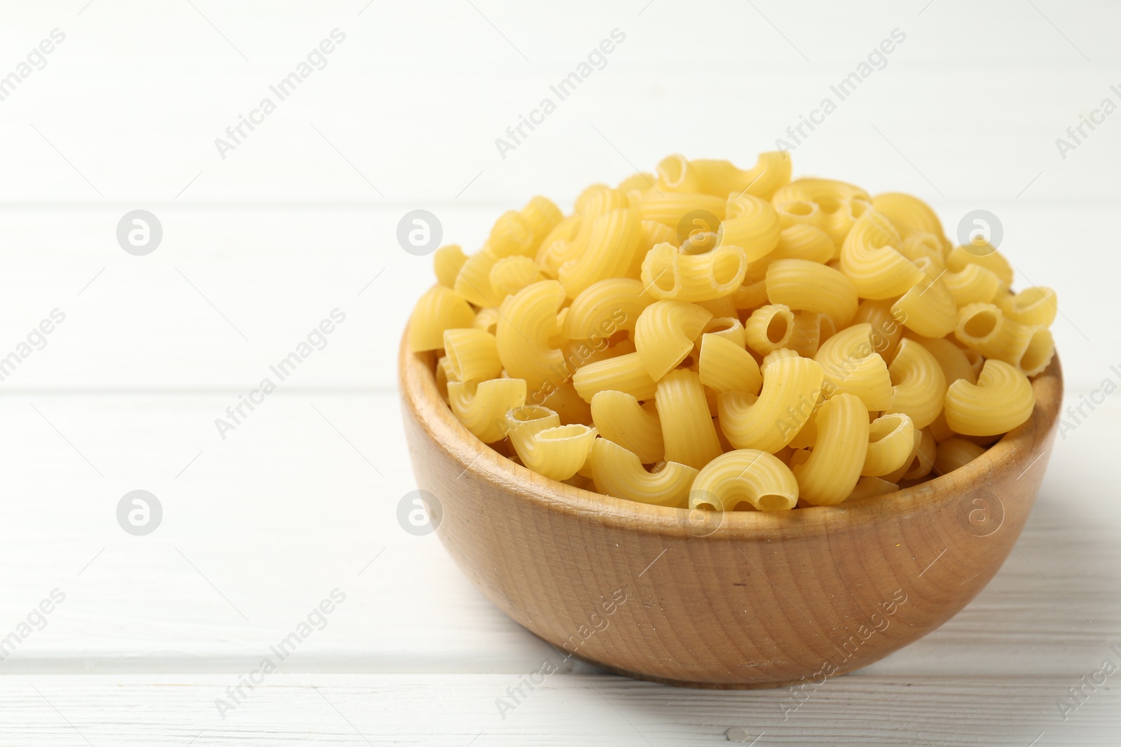 Photo of Raw horns pasta in bowl on white wooden table, closeup. Space for text