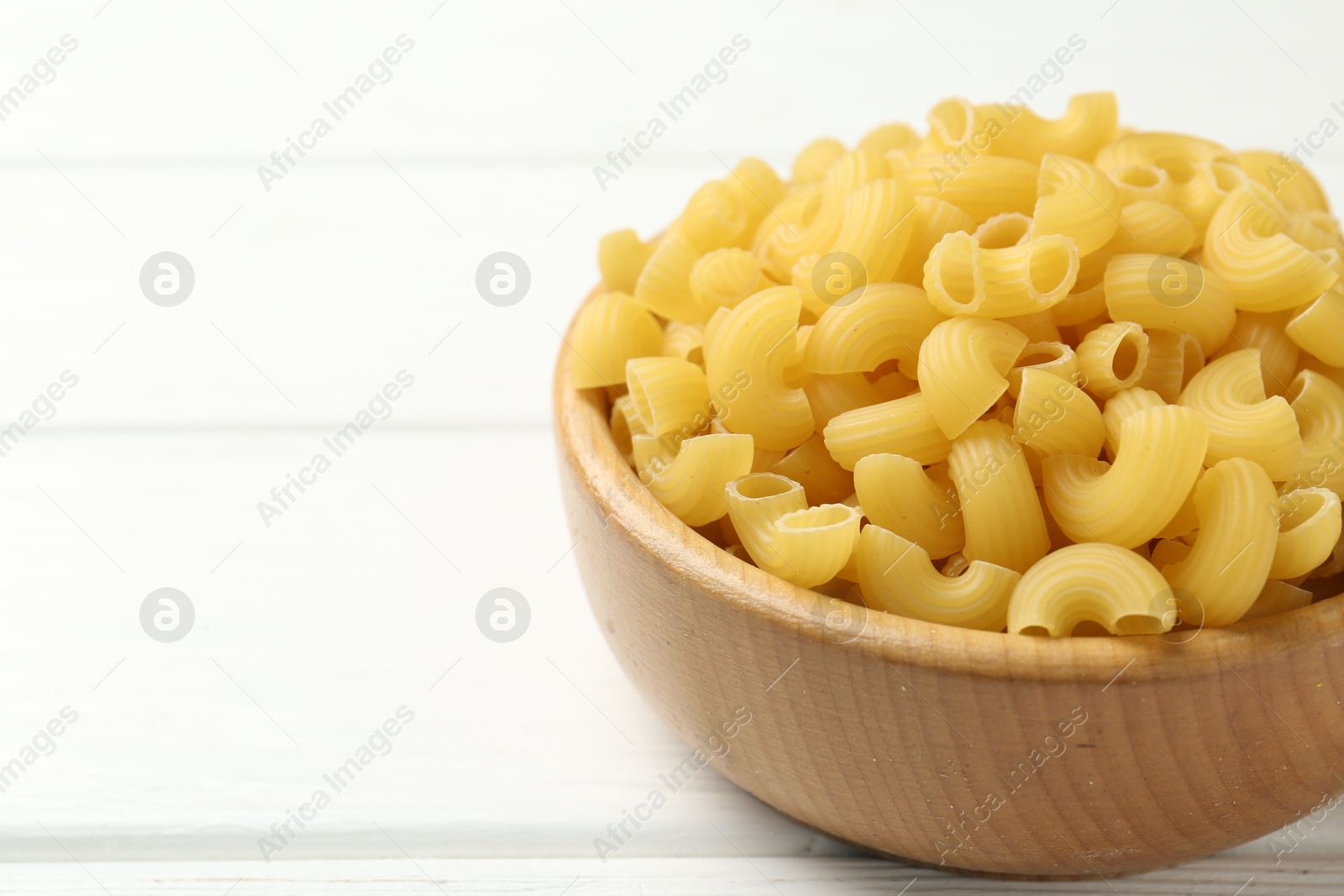 Photo of Raw horns pasta in bowl on white wooden table, closeup. Space for text