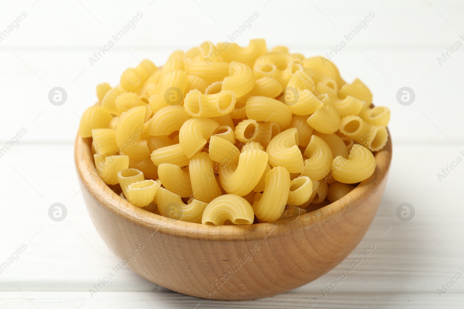 Photo of Raw horns pasta in bowl on white wooden table, closeup