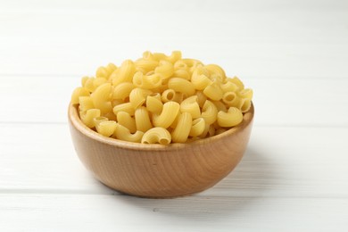 Photo of Raw horns pasta in bowl on white wooden table, closeup