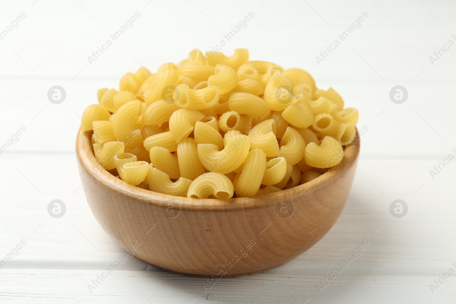 Photo of Raw horns pasta in bowl on white wooden table, closeup