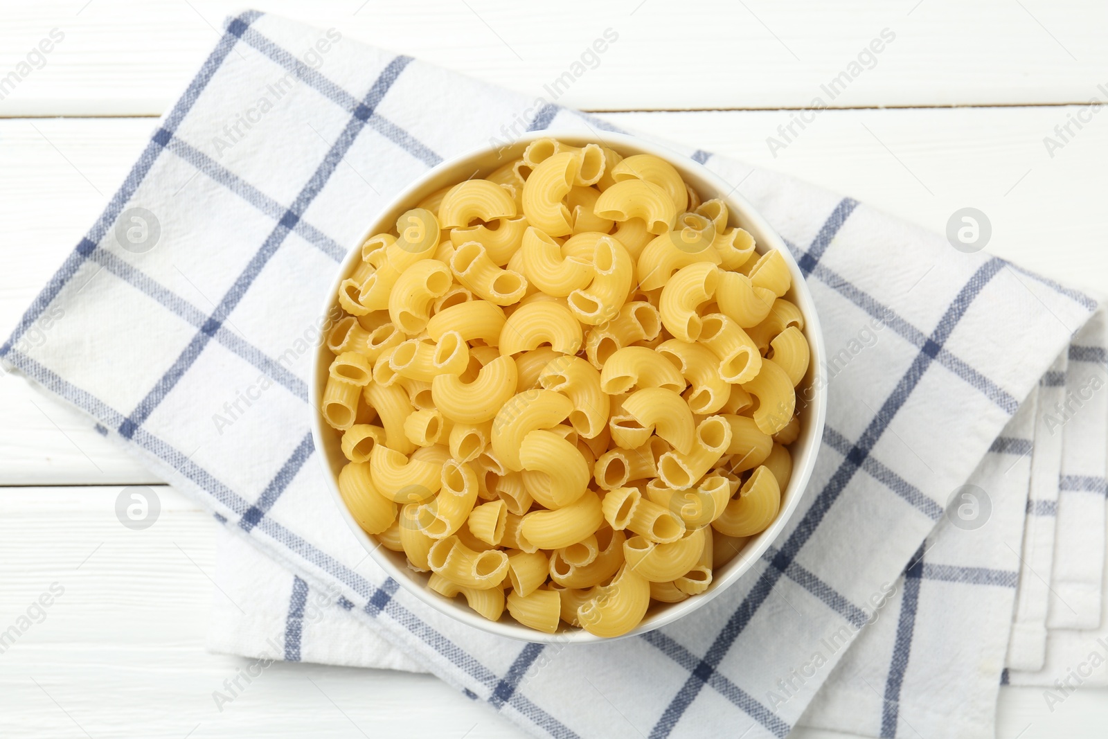 Photo of Raw horns pasta in bowl on white wooden table, top view