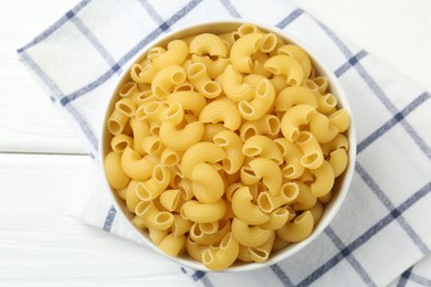 Photo of Raw horns pasta in bowl on white wooden table, top view