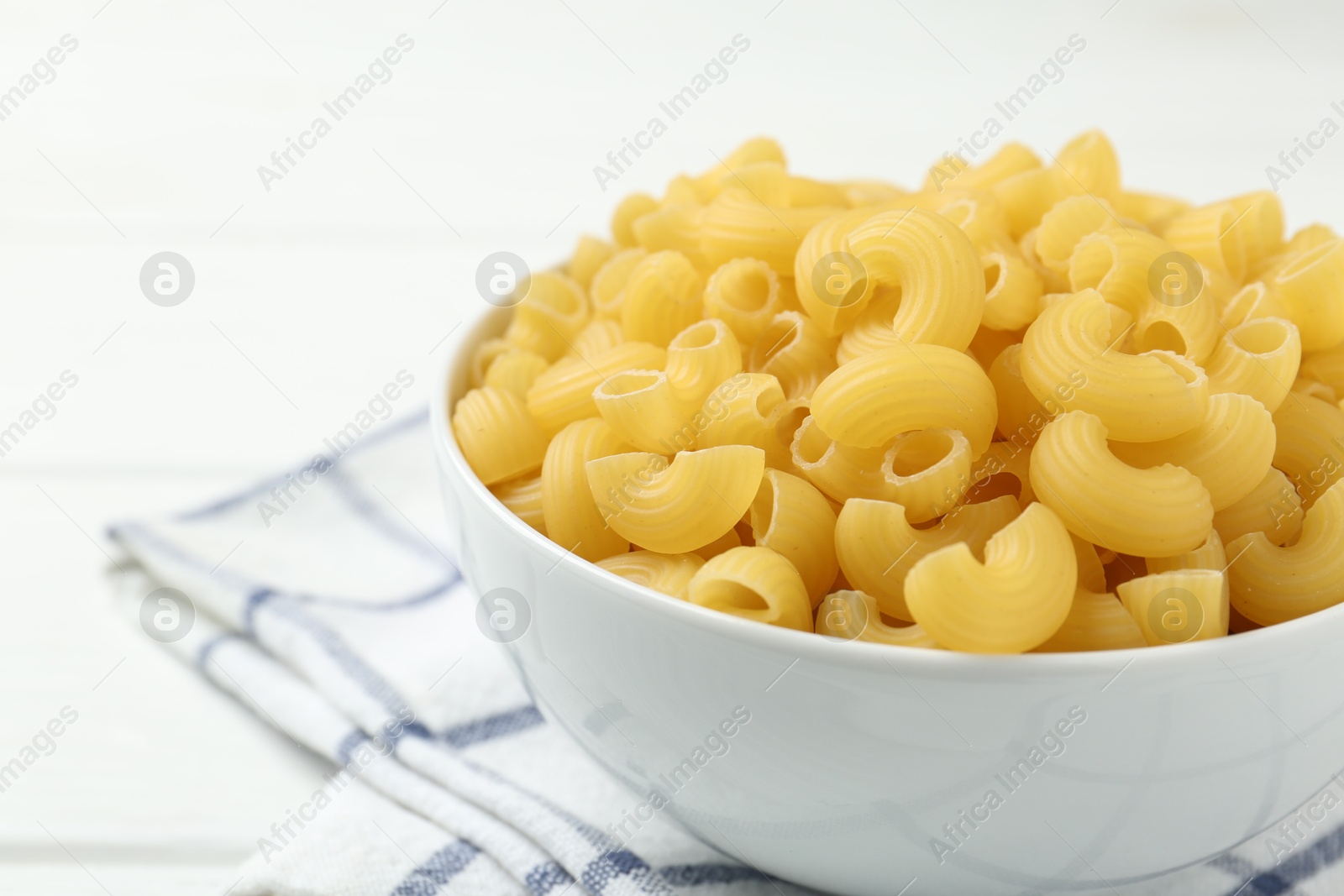 Photo of Raw horns pasta in bowl on white table, closeup