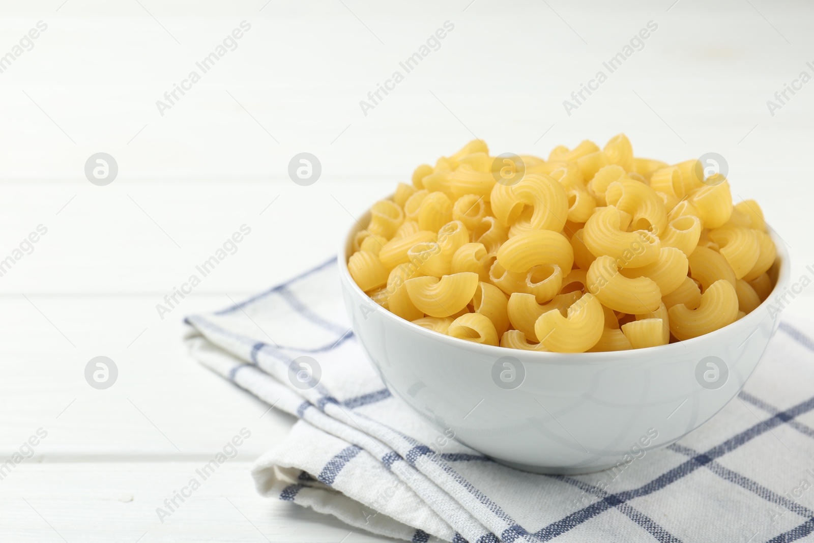 Photo of Raw horns pasta in bowl on white table, closeup. Space for text