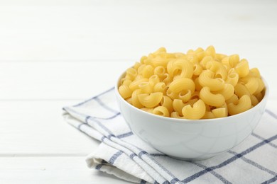 Photo of Raw horns pasta in bowl on white table, closeup. Space for text