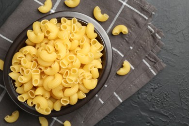 Photo of Raw horns pasta in bowl on black textured table, top view. Space for text