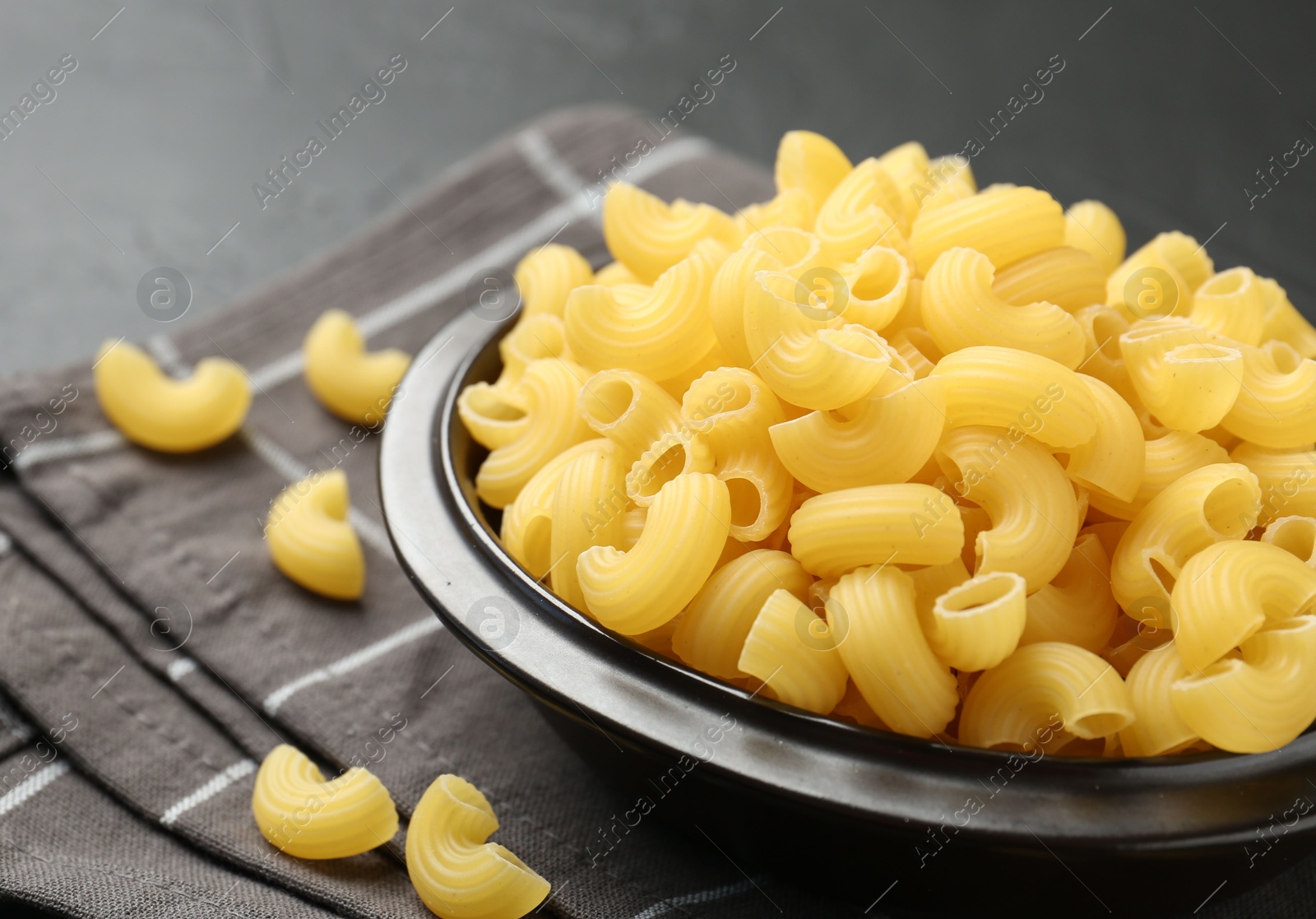 Photo of Raw horns pasta in bowl on black table, closeup