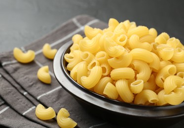 Photo of Raw horns pasta in bowl on black table, closeup