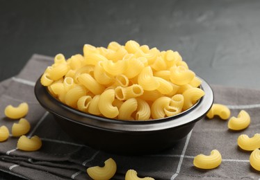 Photo of Raw horns pasta in bowl on black table, closeup