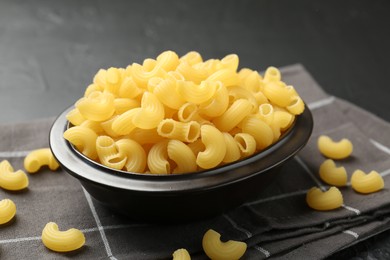 Photo of Raw horns pasta in bowl on black table, closeup