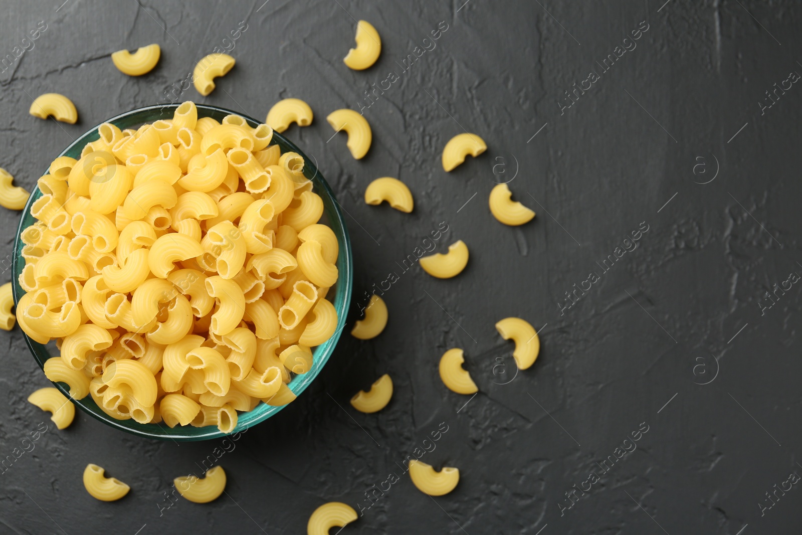 Photo of Raw horns pasta in bowl on black textured table, top view. Space for text