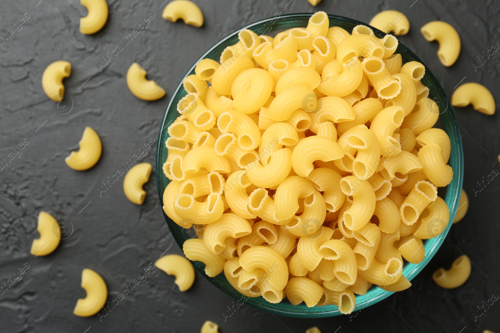 Photo of Raw horns pasta in bowl on black textured table, top view