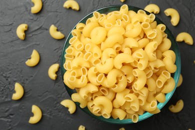 Photo of Raw horns pasta in bowl on black textured table, top view