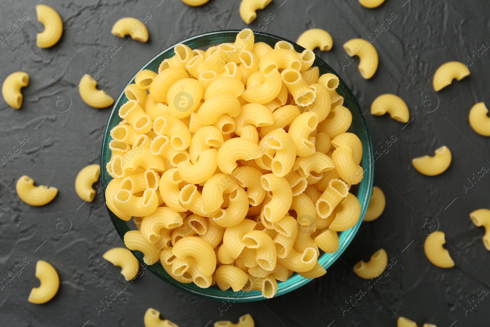 Photo of Raw horns pasta in bowl on black textured table, top view