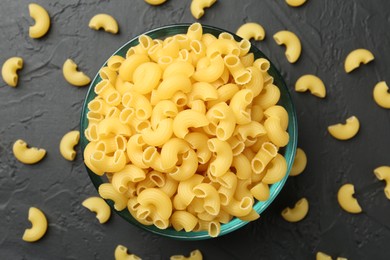 Photo of Raw horns pasta in bowl on black textured table, top view