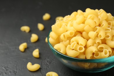 Photo of Raw horns pasta in bowl on black textured table, closeup. Space for text