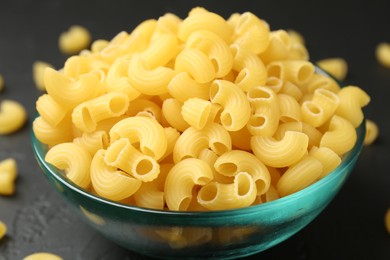 Photo of Raw horns pasta in bowl on black table, closeup