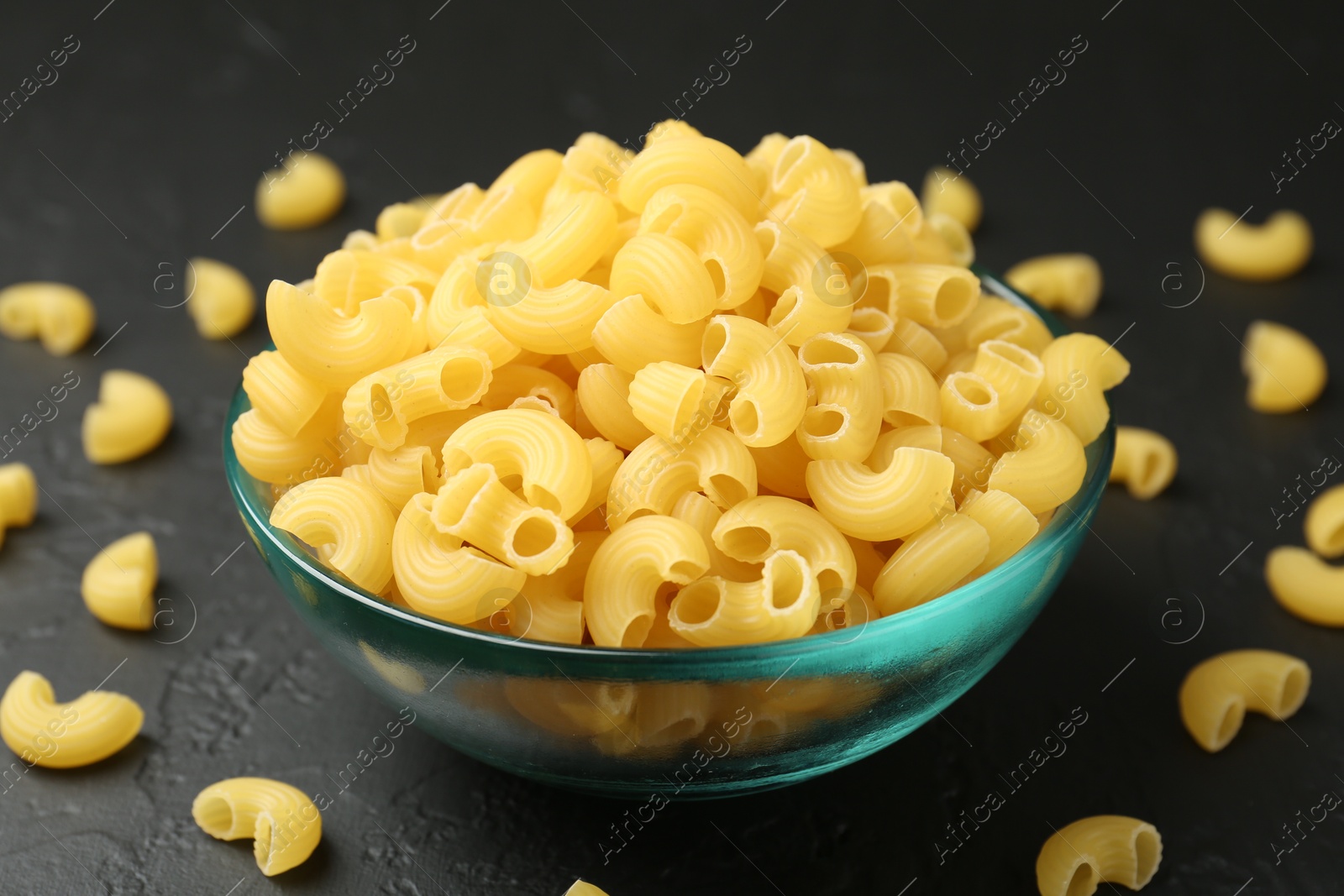 Photo of Raw horns pasta in bowl on black table, closeup