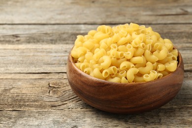 Photo of Raw horns pasta in bowl on wooden table, closeup