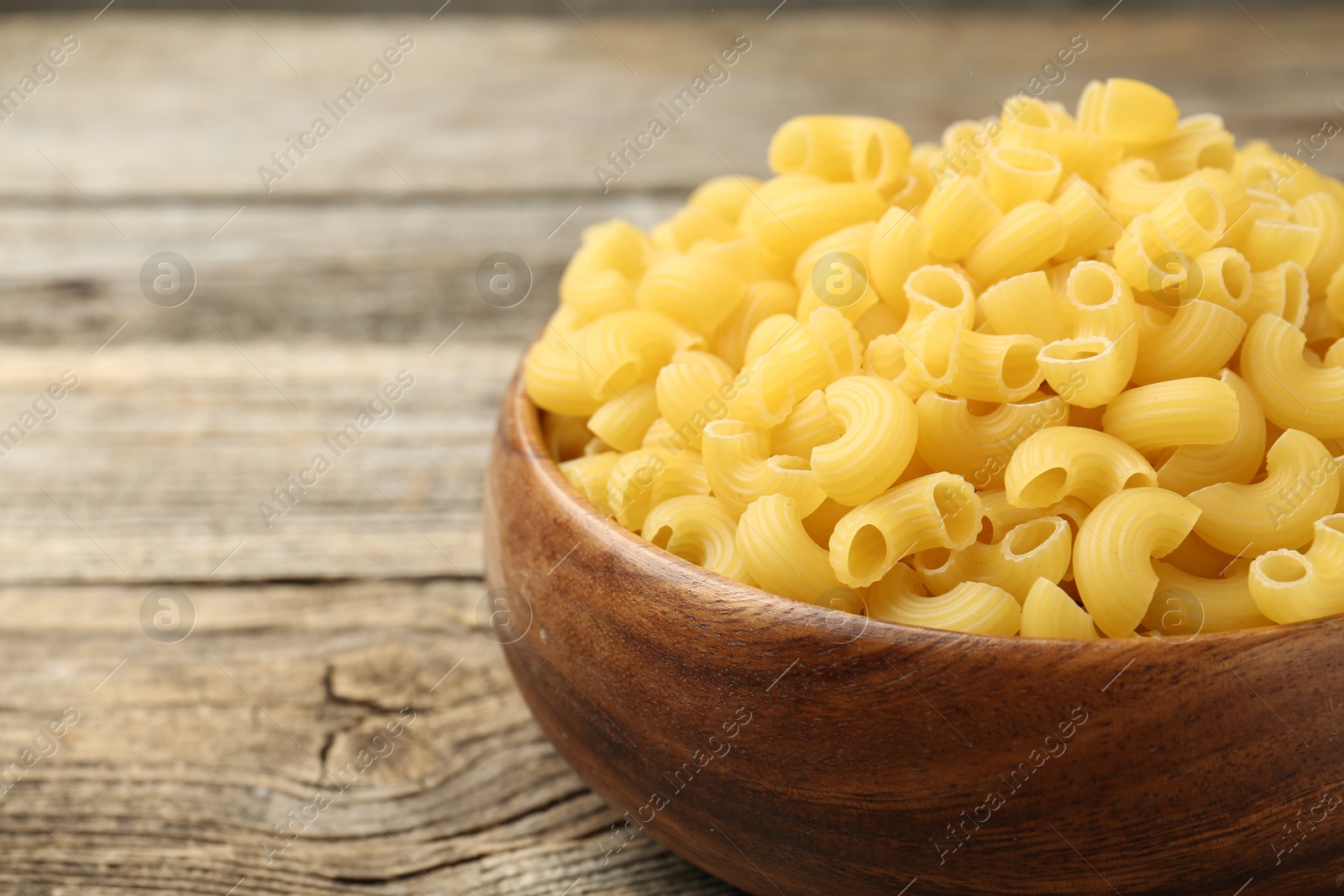 Photo of Raw horns pasta in bowl on wooden table, closeup. Space for text