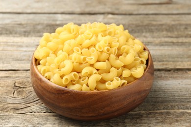 Photo of Raw horns pasta in bowl on wooden table, closeup