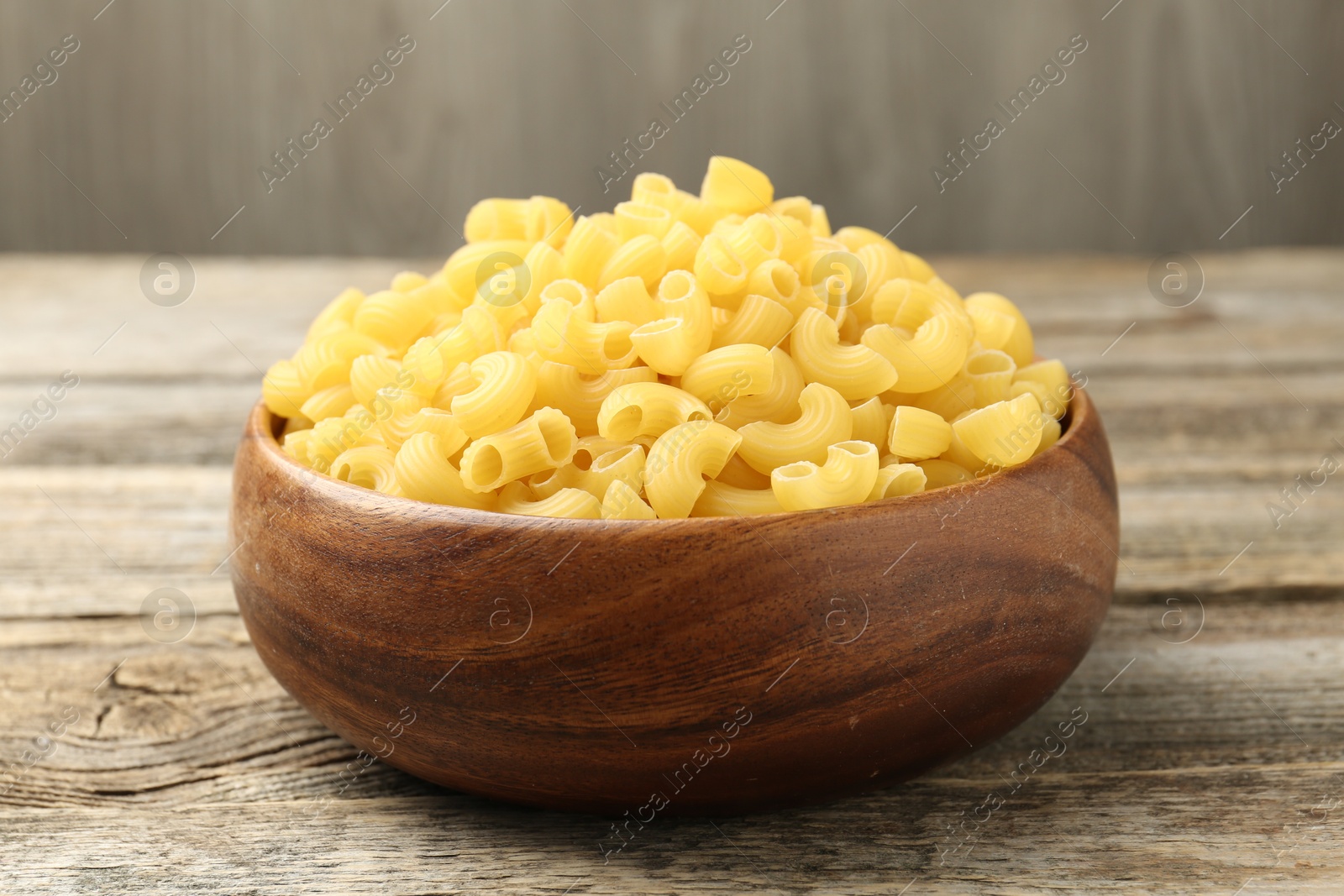 Photo of Raw horns pasta in bowl on wooden table, closeup