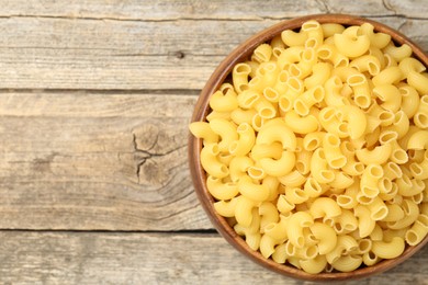 Photo of Raw horns pasta in bowl on wooden table, top view. Space for text