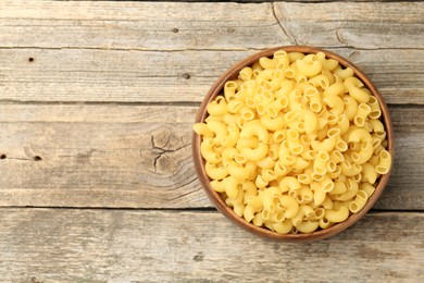 Photo of Raw horns pasta in bowl on wooden table, top view. Space for text