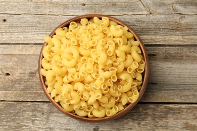 Photo of Raw horns pasta in bowl on wooden table, top view