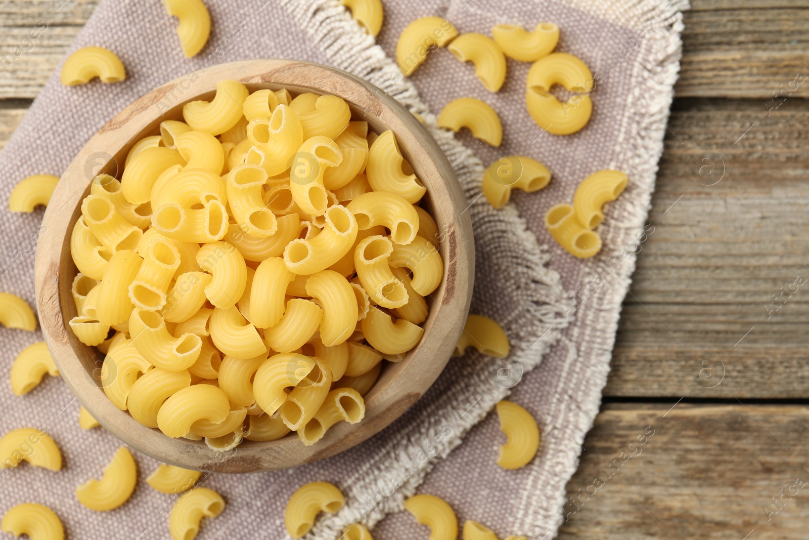 Photo of Raw horns pasta in bowl on wooden table, top view. Space for text