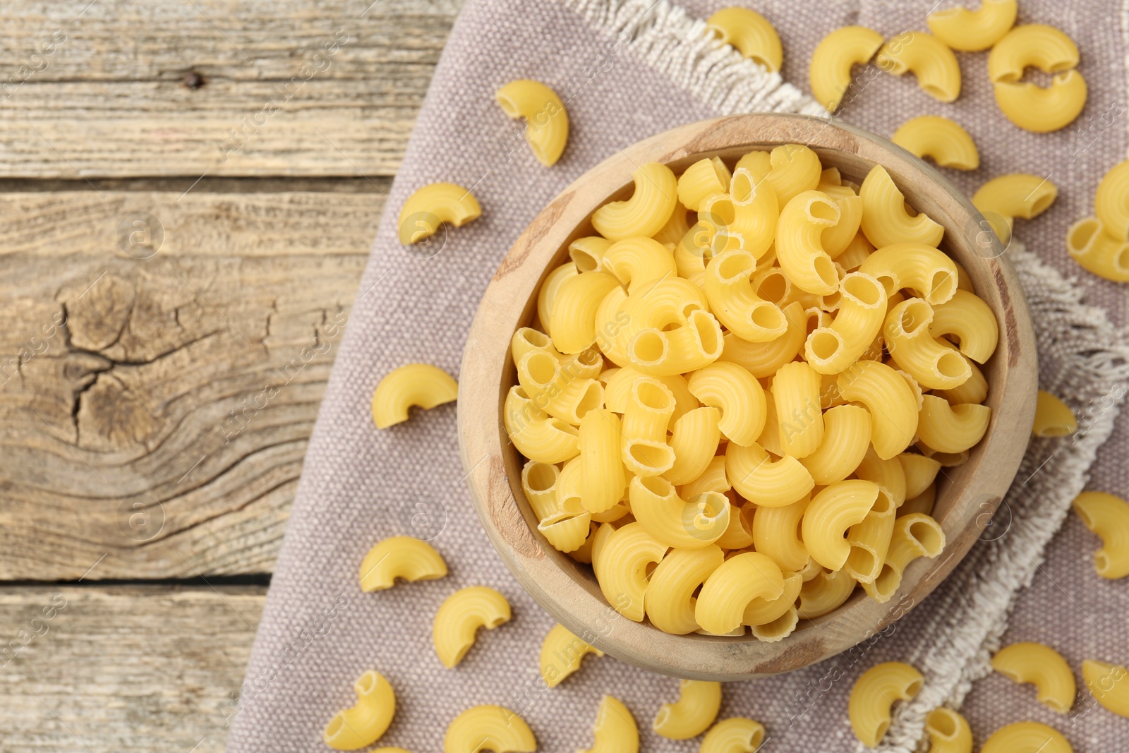 Photo of Raw horns pasta in bowl on wooden table, top view. Space for text