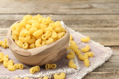 Photo of Raw horns pasta in bowl on wooden table, closeup. Space for text