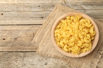 Photo of Raw horns pasta in bowl on wooden table, top view. Space for text