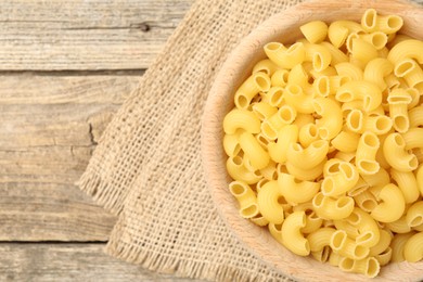 Photo of Raw horns pasta in bowl on wooden table, top view. Space for text