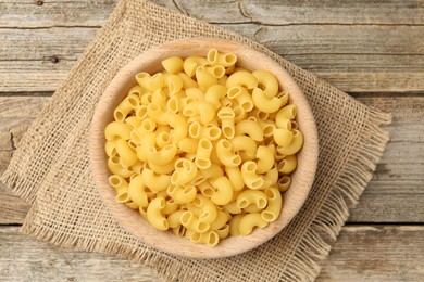 Photo of Raw horns pasta in bowl on wooden table, top view