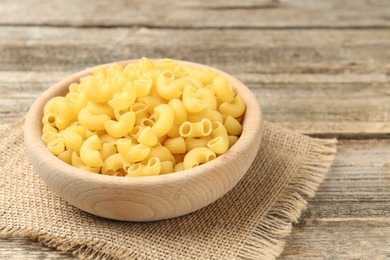 Photo of Raw horns pasta in bowl on wooden table, closeup