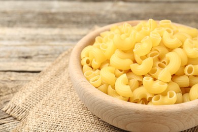 Photo of Raw horns pasta in bowl on wooden table, closeup. Space for text