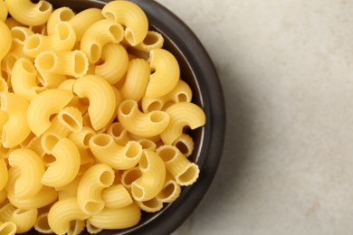 Photo of Raw horns pasta in bowl on gray textured table, top view. Space for text